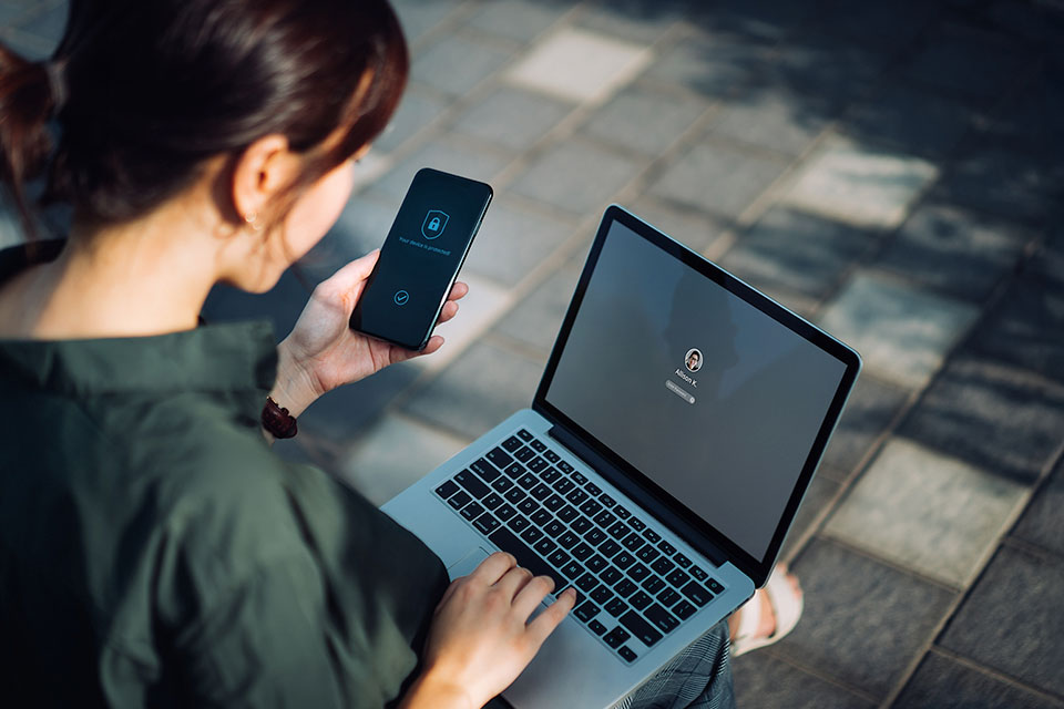 Woman logging into her laptop, using her phone for authentication