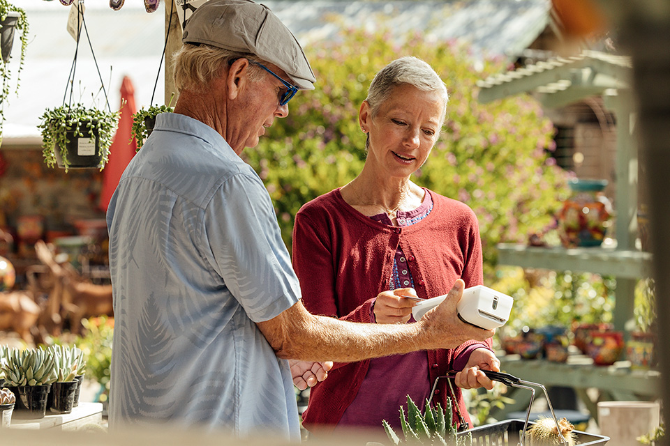 A man holding out a card machine for a woman paying for her shopping