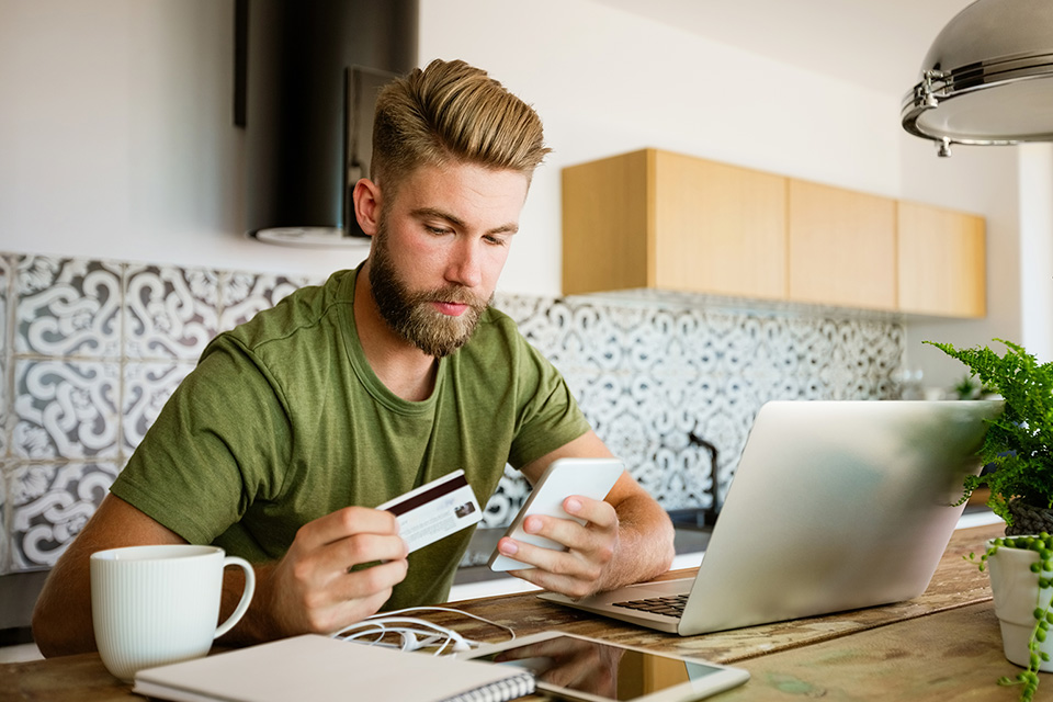 A man sitting at a table holding his phone and debit card
