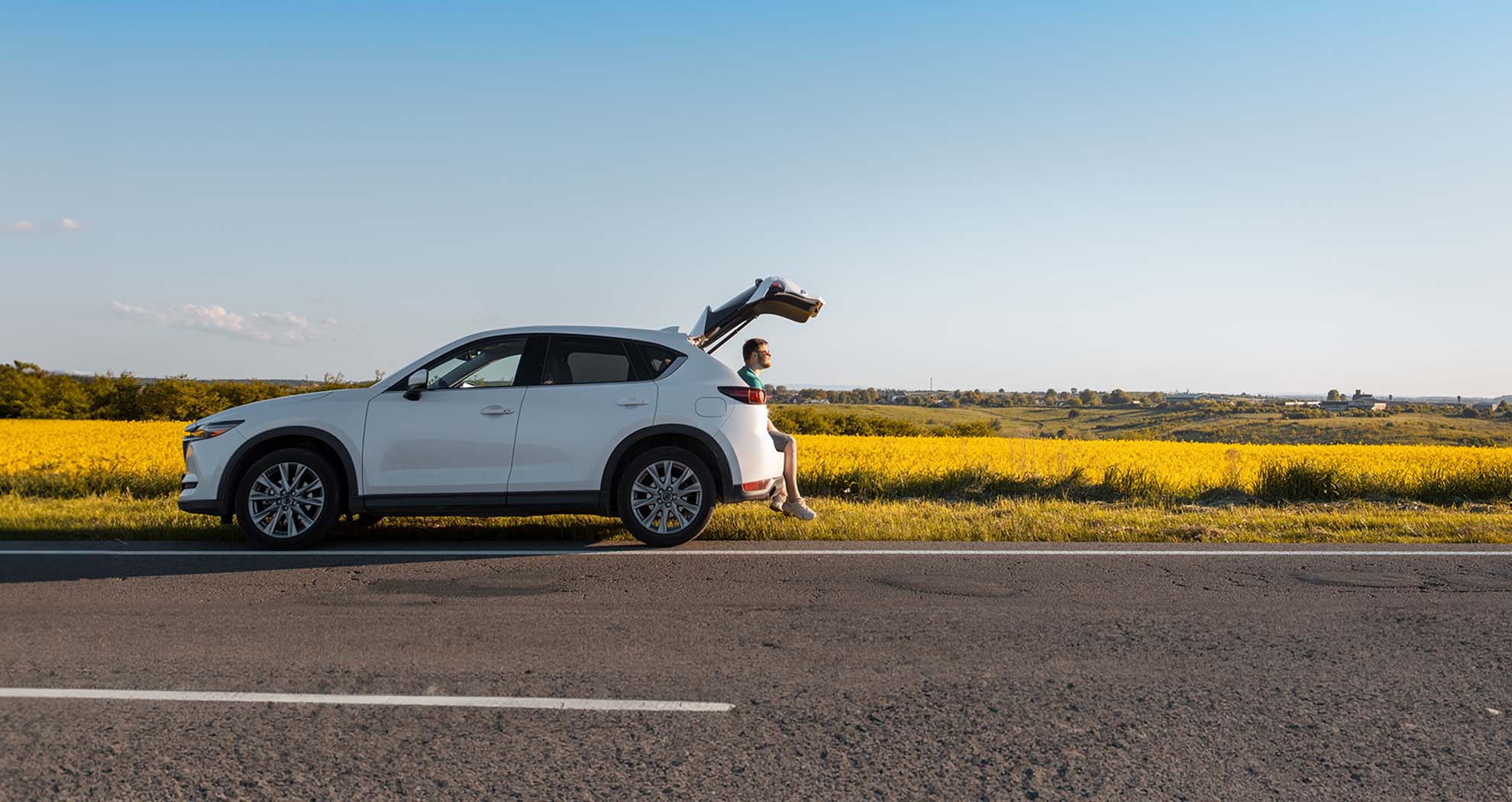 A man siting in the booth of his car pulled over on the side of the road in the country side.