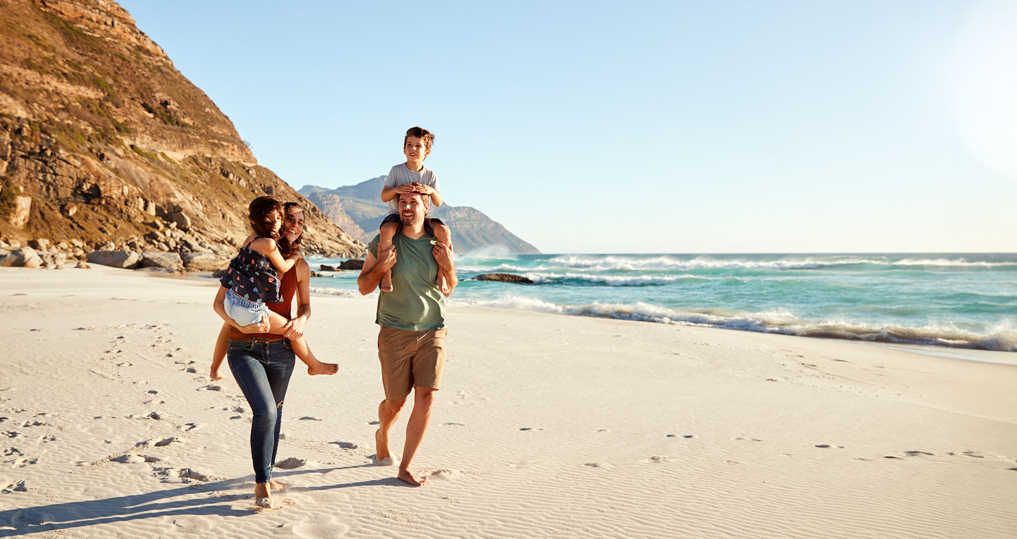 A family of 4 on the beach enjoying their care free vacation, covered by AIB travel insurance.