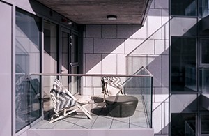 Glass apartment balcony with chair and stool in sunlight