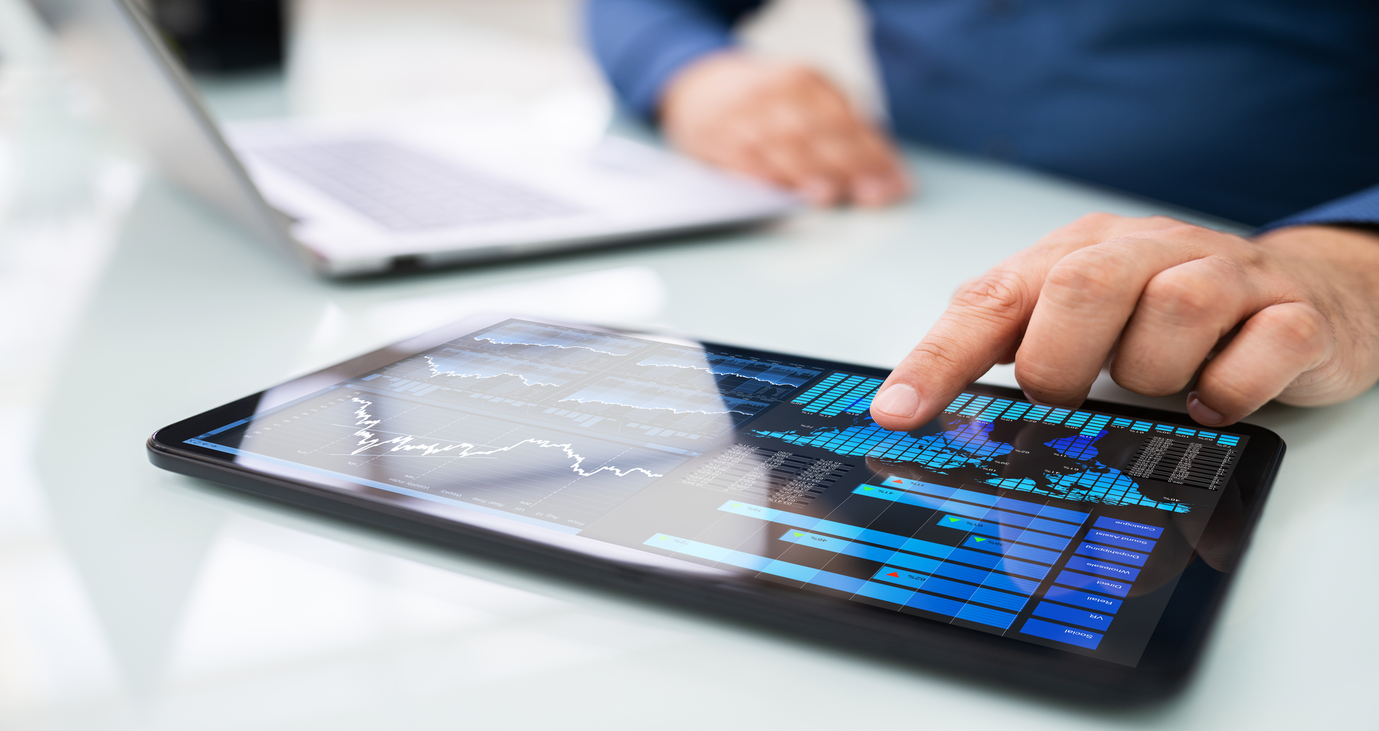 Close up of a finger pressing a tablet screen displaying markets