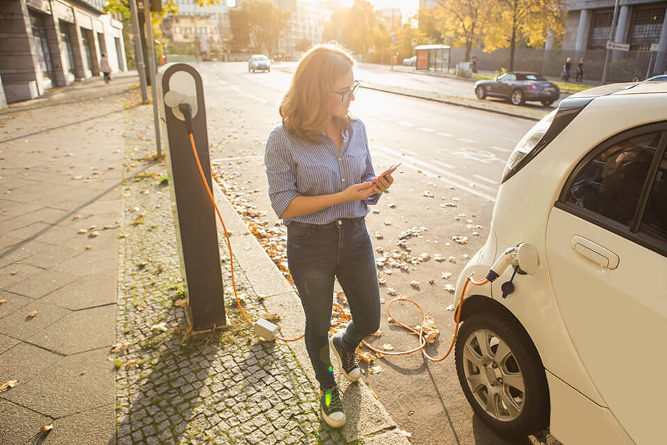 A woman setting up her car to charge on the street.