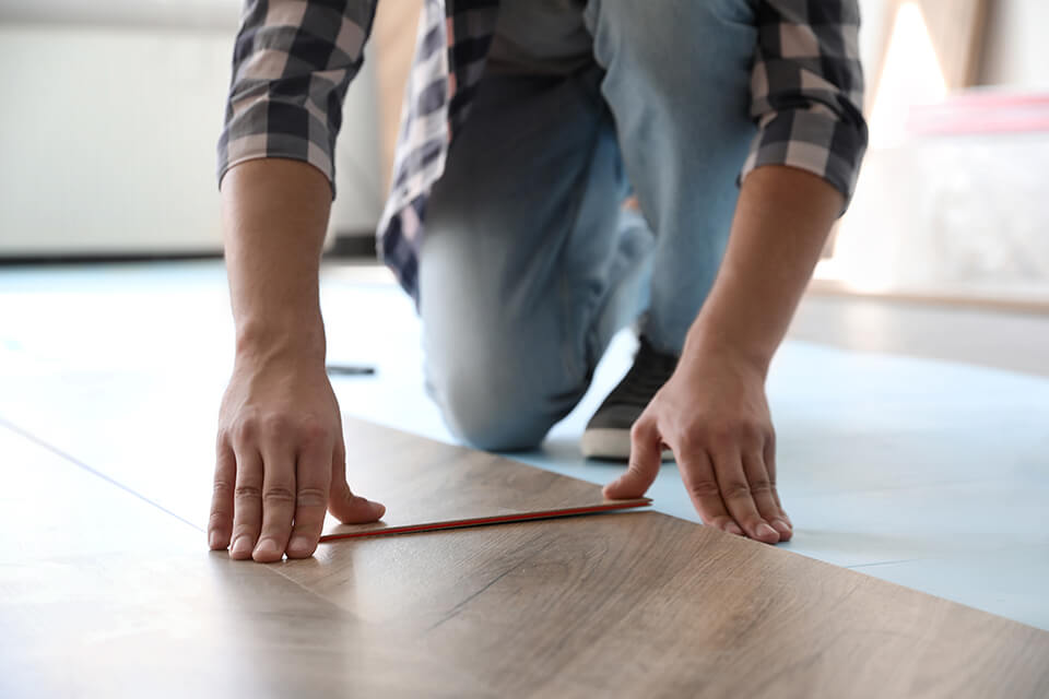 A man measuring the width of a floor board.
