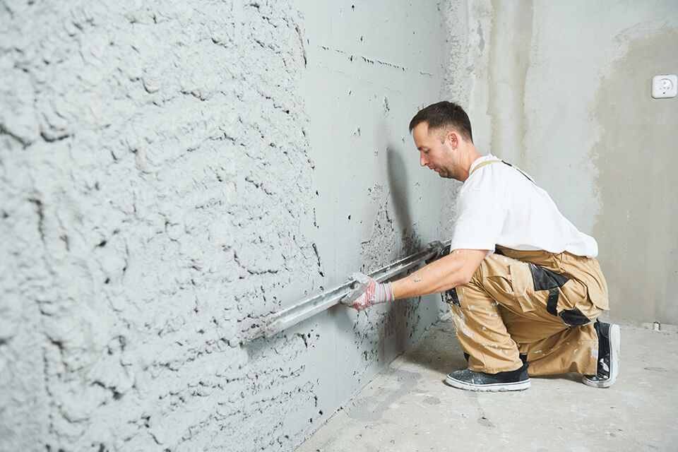 A man smoothening out a platestered wall.