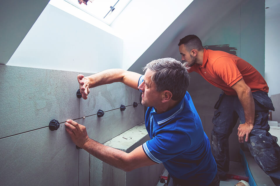 Two men installing wall tiles.