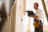 A construction worker drilling a hole in a wall inside a house.