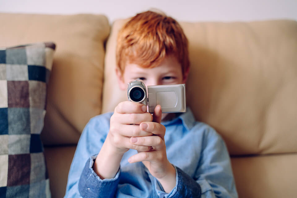 A close up of a boy on a sofa using a video camera .