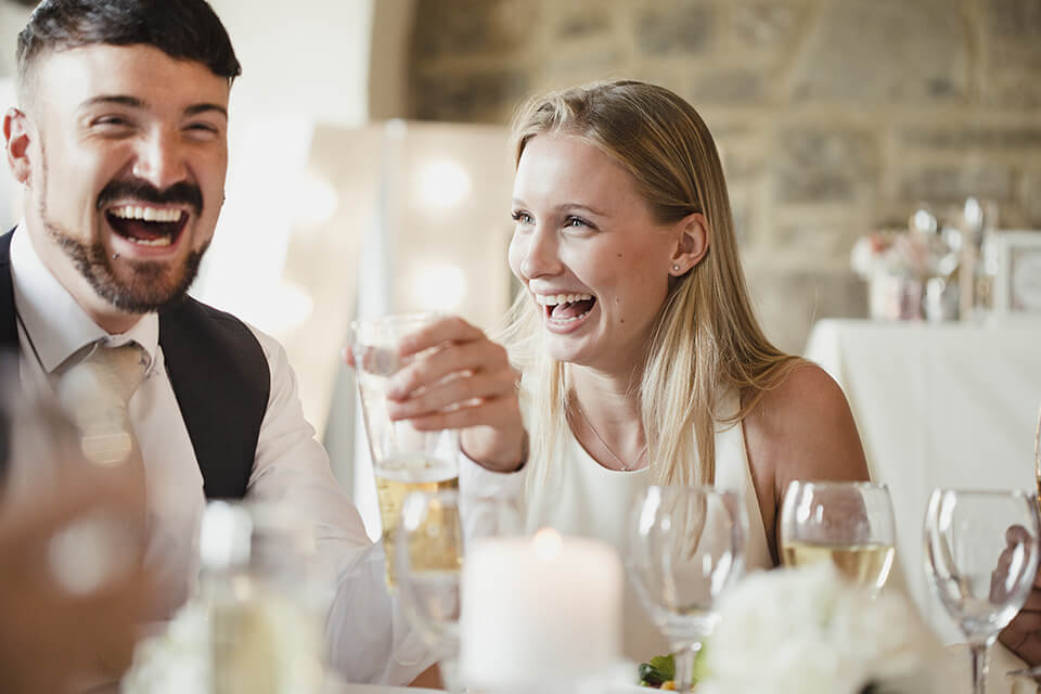 A couple laughing together while dressed very fancy drinking champagne in a nice restaurant.