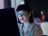 Woman sitting at a computer with the screen reflected in her glasses.
