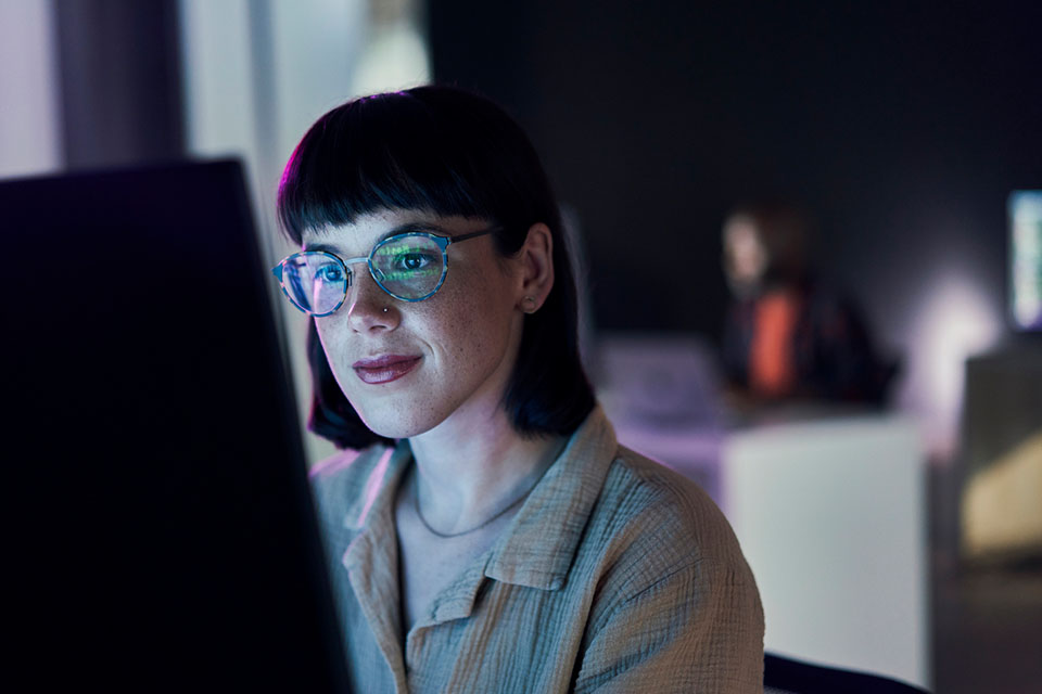 Woman looking at computer with screen reflected in her glasses.