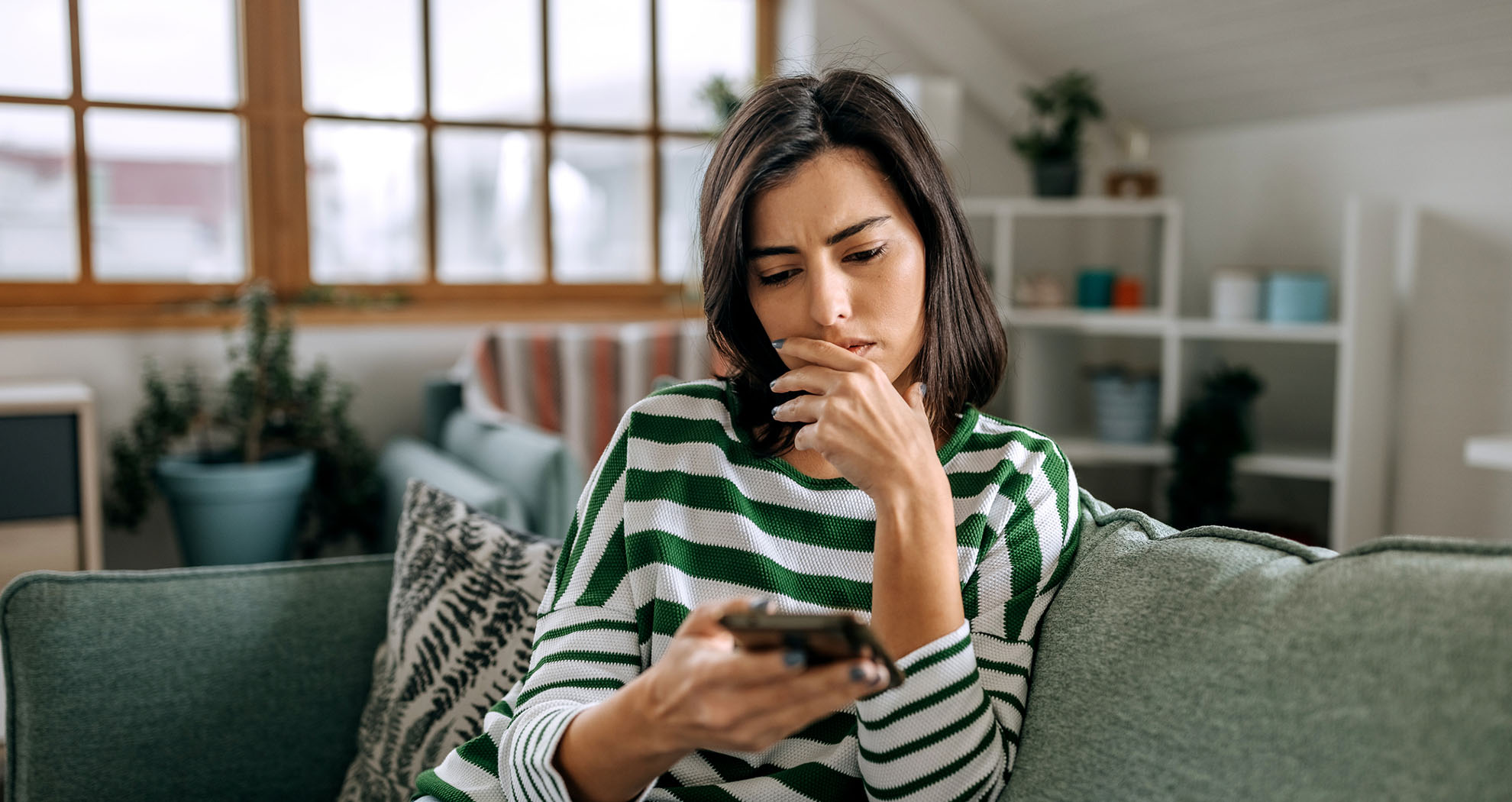 Woman in her living room reading about common frauds on her phone.