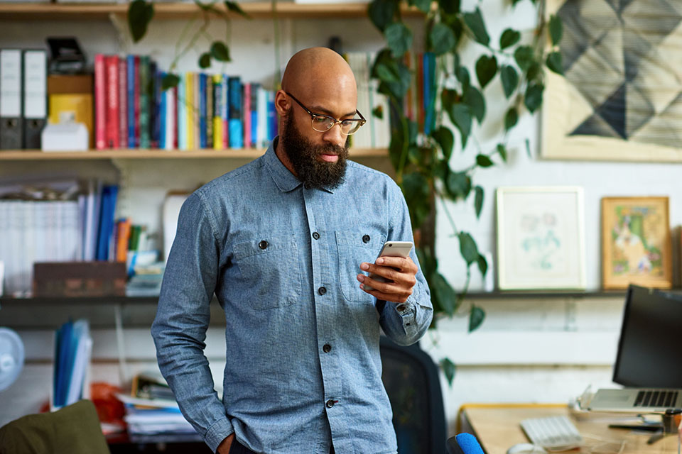 A man standing next to a desk looking at his phone.