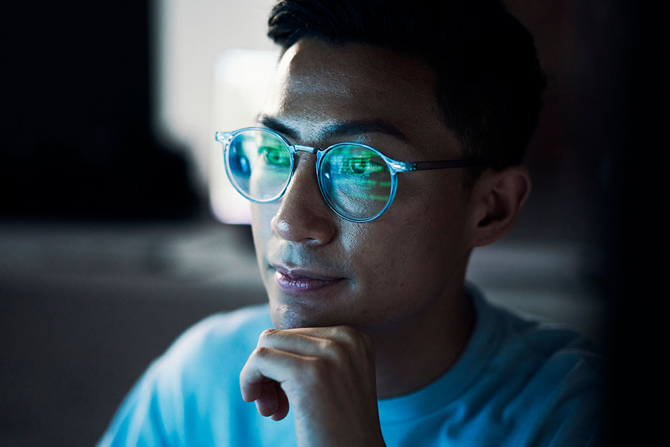 Man looking thoughtfully with computer screen reflected in his glasses.