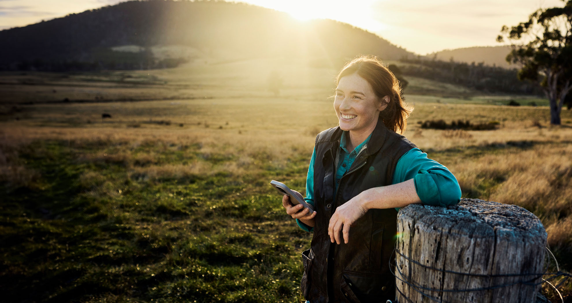 Woman smiling in a field holding her phone.