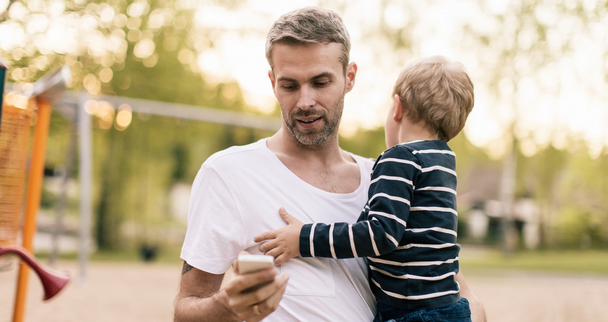 Man holding his son while looking at his phone.